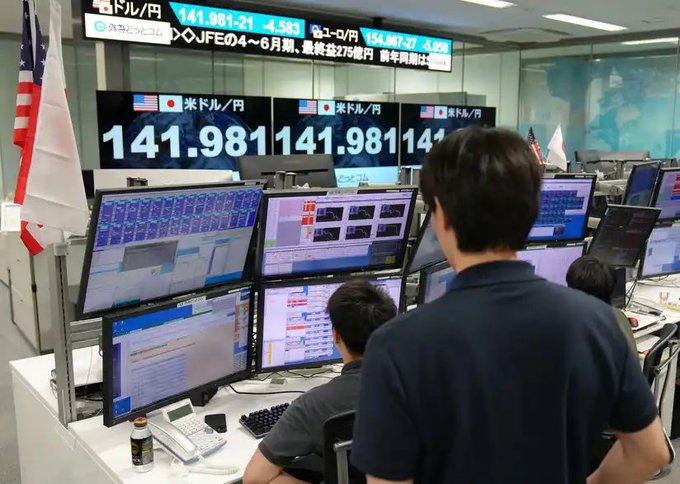 A financial trading floor in Japan with a large electronic board showing USD/JPY exchange rate of 141.981 (down -4.583), with traders working at multi-monitor workstations displaying various trading screens and an American flag visible on the left.
