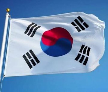 South Korean flag waving against a clear blue sky, featuring the white background with red and blue taegeuk symbol in the center and four black trigrams in the corners.