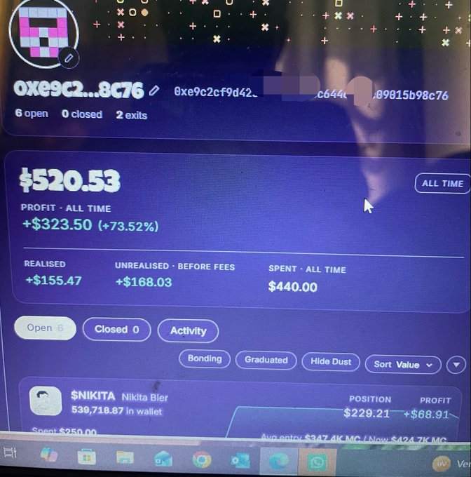 A computer monitor displays a crypto wallet dashboard showing a profit of $520.53 with a +73.52% gain, including an entry for '$NIKITA Nikita Bier' with 539,718.87 in wallet.
