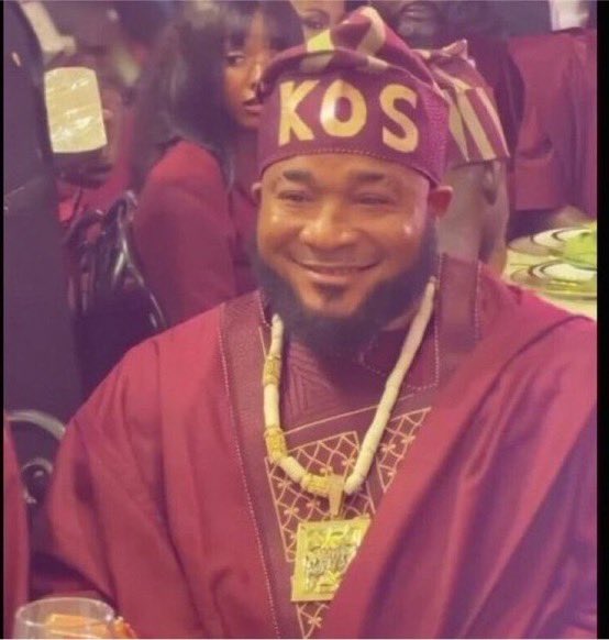 A smiling man wearing a maroon traditional outfit with coral beads and a cap embroidered with "KOS" attends a lively event. The post appears to be a giveaway promotion, likely using the image to attract engagement from followers.