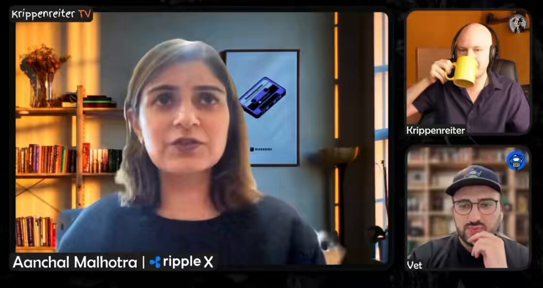 The image shows a group of people sitting around a table, with one person drinking coffee from a mug while another person has their hand up to their face as if they are about to speak or make a gesture. The background features a bookshelf filled with various books and a vase on the shelf. A caption below the image reads "I would like XRP to become indispensable".