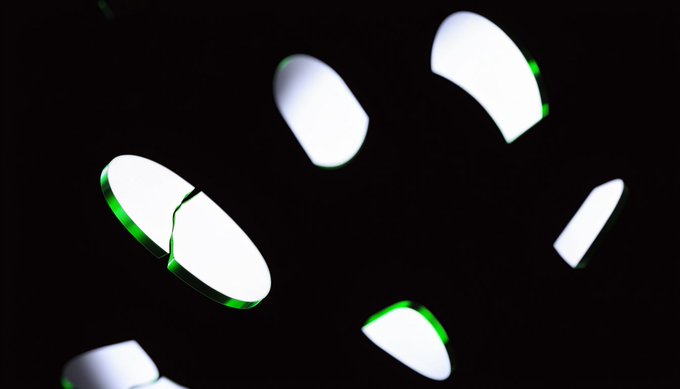 A dark image featuring scattered curved white shapes with green edges against a black background, resembling broken pieces or abstract reflections.