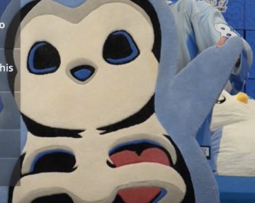A flat, stylized cutout of a cartoon penguin character with large blue eyes, displayed at what appears to be an anime convention booth.