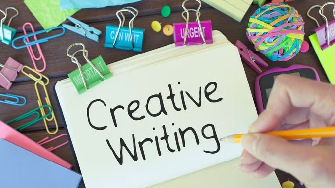 The image features a white piece of paper with the word "CREATIVE WRITING" written on it, along with a hand holding a pencil above it. The background includes various office supplies such as pens, pencils, and staplers, suggesting that this is an environment where writing or creative work takes place.