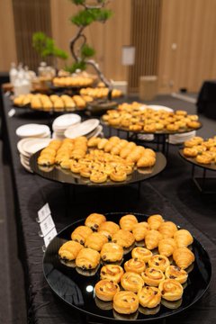 Black plates display an assortment of pastries, including egg tarts and small buns, on a table.