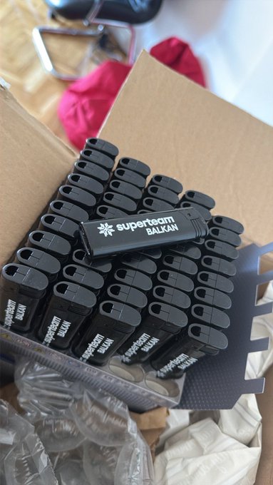 An open cardboard box filled with numerous black 'superteam BALKAN' branded USB flash drives.
