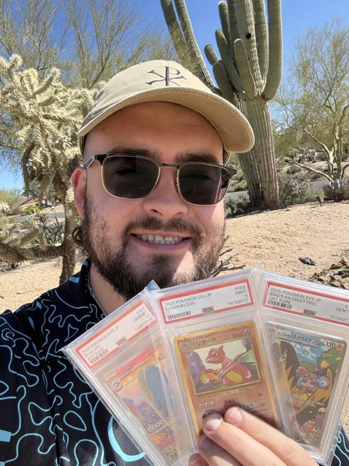 A man wearing a cap and sunglasses holding up three graded PSA Pokémon cards, including Charmeleon and a Japanese card, outdoors with cacti in the background.