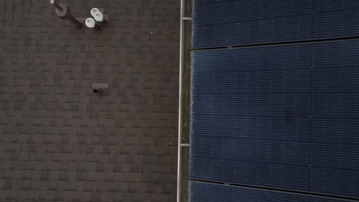 The image shows a rooftop with two solar panels installed. The panels are black and have a grid-like pattern. There are also two white buckets placed near one of the panels, possibly for collecting rainwater or storing solar energy.