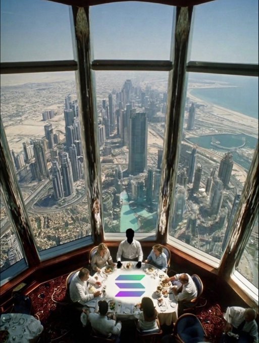 The image shows a group of people sitting at a table with food, likely enjoying a meal together. They are seated around a dining table that has a centerpiece featuring a large "SOLANA" logo. The restaurant appears to be located on top of a skyscraper or in an elevated position, as evidenced by the panoramic view of the city through the windows.

The people at the table seem to be engaged in conversation and enjoying their time together. There are several chairs around the dining table, with some empty ones nearby. The overall atmosphere appears to be relaxed and social, with everyone gathered for a meal and a shared experience.