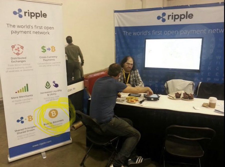 Two men sit at a booth for Ripple, "The world's first open payment network," discussing business over a table with pastries.
