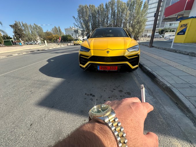 A hand wearing a gold Rolex watch and bracelet holds a cigar in the foreground, with a yellow Lamborghini Urus parked behind it—likely symbolizing the luxury lifestyle being given away. The post references "Solana addresses ASAP, lets bless 3 winners," indicating a giveaway where participants provide their crypto wallet addresses for a chance to win.