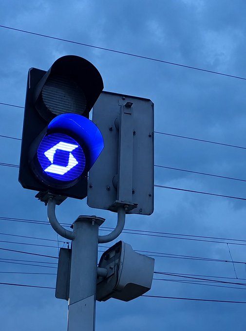 A blue traffic light displaying the number "6" hangs against a cloudy sky, with power lines visible in the background. The accompanying text "红灯停 SafePal 行" translates to "Stop at red lights, SafePal goes," playfully pairing the traffic signal imagery with a message promoting the SafePal crypto wallet.