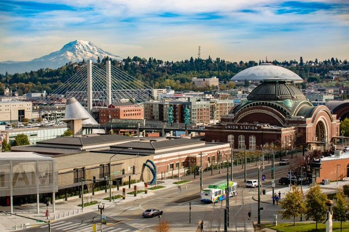 An aerial view of Tacoma showing Union Station with its distinctive dome, a bridge, downtown buildings, and Mount Rainier in the background.