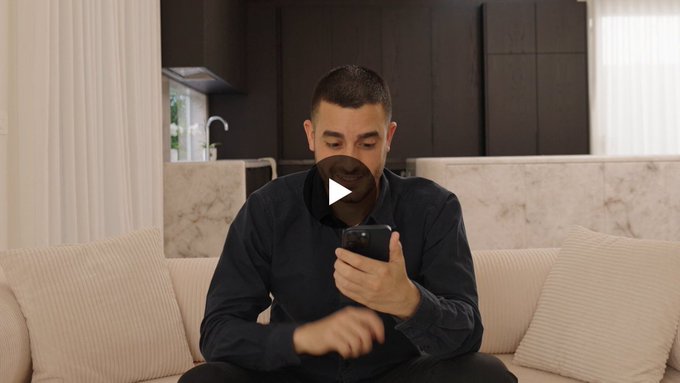 A man sits on a couch looking at his phone, appearing tense as he decides whether to cash out his bet, which relates to the post's theme of deciding the highest multiplier one would risk in the Stake Pump game.