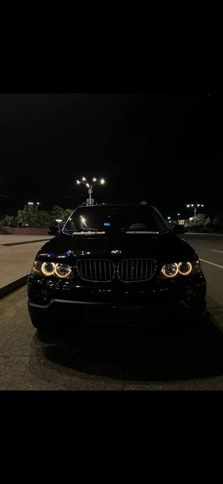 A nighttime photo of a black BMW SUV parked in a lot with its headlights and signature angel eye rings illuminated.