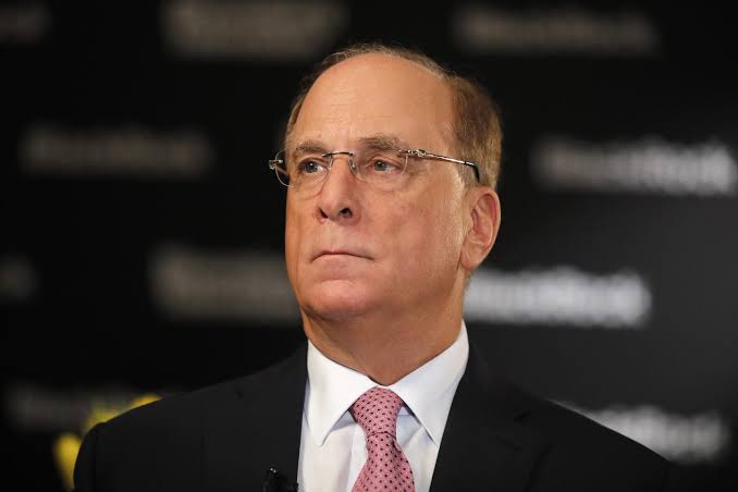 Larry Fink, CEO of BlackRock, listens attentively at an event with branded text visible on the dark backdrop behind him. The image ties into the post about BlackRock's ETFs moving $232.2M into Bitcoin and $192.4M into Ethereum, totaling over $424M in inflows.