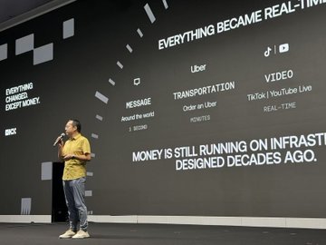 A man in a yellow shirt speaks on stage in front of a large screen displaying text including "EVERYTHING BECAME REAL-TIME," "Uber," "MESSAGE," "TRANSPORTATION," "VIDEO," and "MONEY IS STILL RUNNING ON INFRASTRUCTURE DESIGNED DECADES AGO," which visually complements the post's discussion of real-time tokenized stock trading and infrastructure for RWA products on OKX.