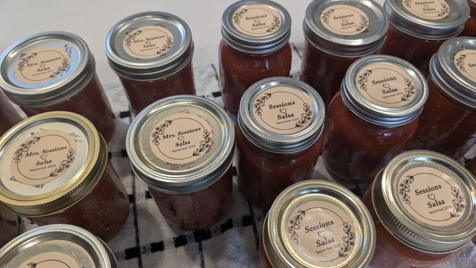 A collection of homemade salsa jars labeled "Mrs. Sessions Salsa" are arranged on a checkered towel, showing the busy canning work of @MrsSessions.