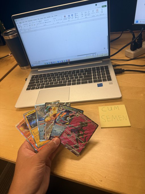 A hand holding Pokémon cards in front of an HP laptop displaying Excel, with a sticky note reading 'CUM SEMEN' on the desk.
