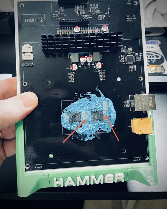 A hand holds up a 'THOR P2' circuit board labeled 'HAMMER' at the bottom, with red arrows pointing to chips covered in blue thermal paste.