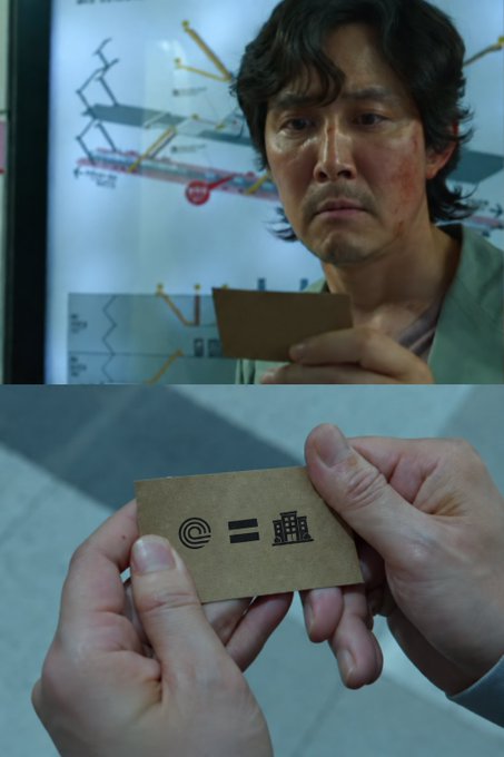 The image shows a scene from Squid Game featuring the Front Man (Lee Byung-hun) examining a card with symbols: a circle, an equals sign, and a triangle, corresponding to the circle, triangle, and square player shapes.
