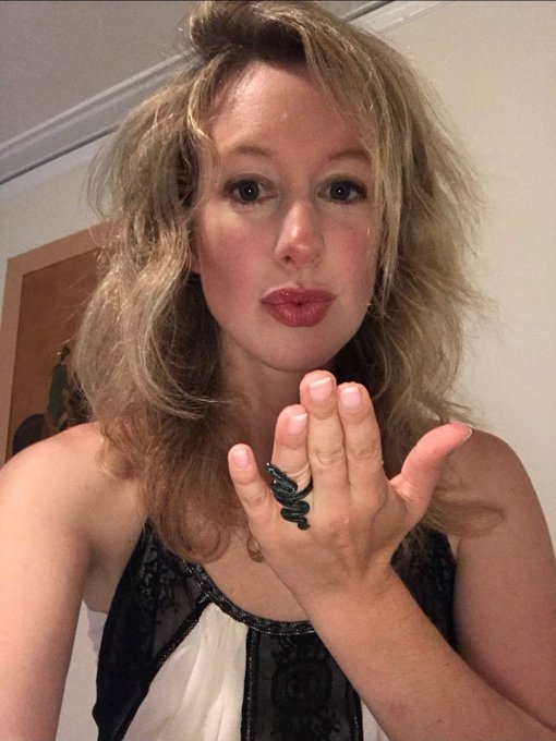 A selfie of a woman with blonde hair puckering her lips and holding up her hand to display a snake-shaped ring, wearing a black and white top.