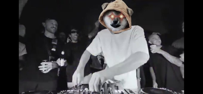 A person wearing a dog mask with glowing red star eyes DJs at a mixer while a crowd watches in a dark venue.