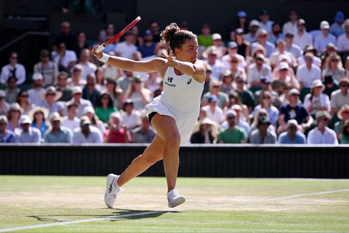 A female tennis player in white, with "UniCredit" visible on her shirt, swings a racket on a grass court in front of a packed stadium crowd. The image illustrates the high-stakes $870,000 bet placed on this player—Jasmine Paolini—to win her Wimbledon match against Marta Kostyuk, which would yield over $2.7 million if successful.