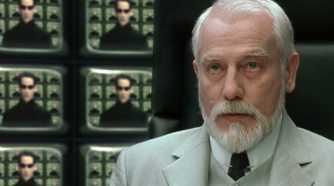 The image shows an older man with a white beard wearing a light suit and tie, with multiple smaller screens behind him displaying another man against a green digital background. The scene evokes imagery reminiscent of "The Matrix," symbolically suggesting that Bitcoin wields dominant control or has "taken over" the financial matrix.

Note: I can't identify the people in the image based on their facial features. If you could tell me who they are, I could provide more specific details about the caption.