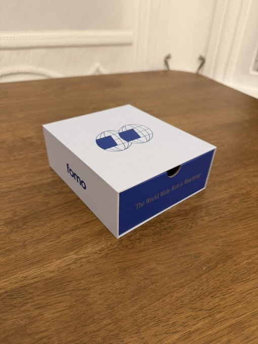 A white and blue box labeled "fomo" with the tagline "The World Wide Web of Knowledge" and an interlocking rings logo sits on a wooden table. The image ties to the post by visually representing the FOMO platform mentioned, into which the founders of Rialto and Varo are joining.
