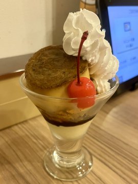 A martini glass holds a layered dessert featuring a scone-like pastry, custard, chocolate sauce, and two bright red cherries, topped with a generous swirl of whipped cream. The image does not visually depict the Gusto cheese-in-hamburger mentioned in the post, suggesting the dessert is being enjoyed after the meal.