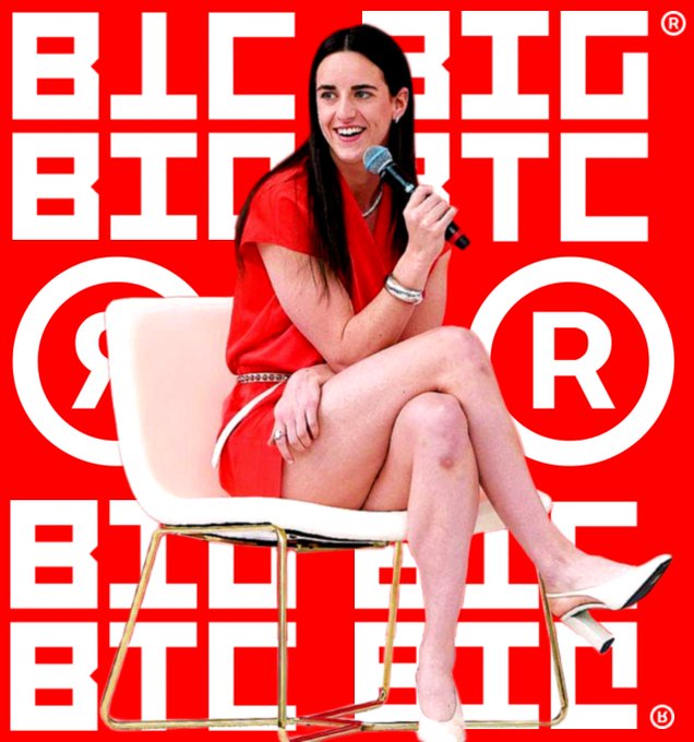 A woman with long dark hair, wearing a red dress and white heels, sits on a modern white chair holding a microphone and smiling, set against a red backdrop featuring the repeated "BLCBTC" and "R" logos. The bold branding and striking red color scheme visually echo the "Compliance Is Defiance®" message, projecting confidence and nonconformity.