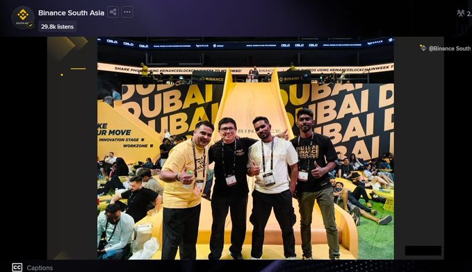 A screenshot of a Binance South Asia livestream showing four men posing together in front of a yellow 'DUBAI' backdrop at the Binance Blockchain Week event, with 29.8k listeners.