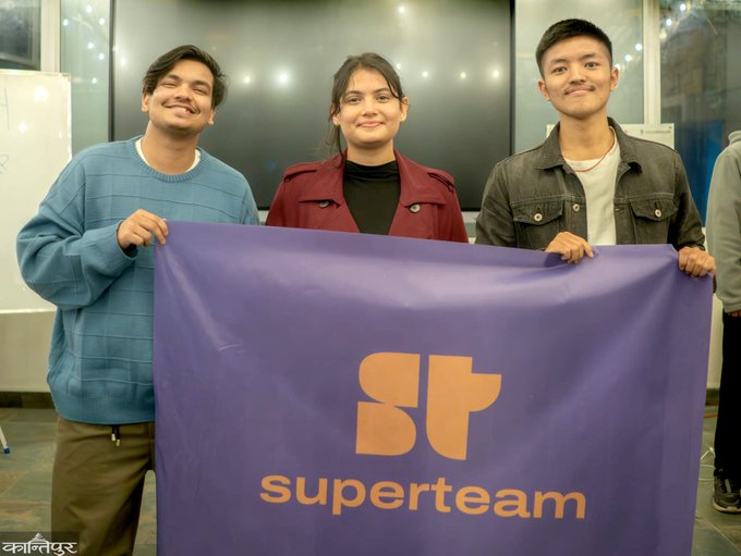 Three young adults smile and hold up a purple "superteam" banner featuring an orange 'ST' logo.