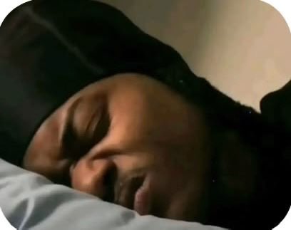 A close-up photo of a person sleeping peacefully with their head on a white pillow against a dark background.