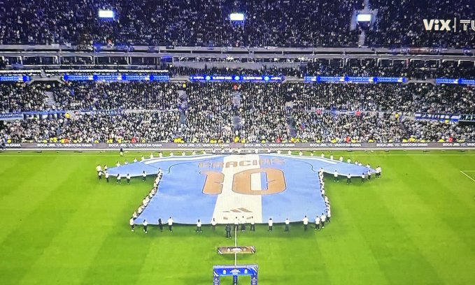 A massive #10 Messi jersey is unfurled on the pitch at a packed stadium ahead of Argentina's match against Benin, with players and officials gathered around the light blue and white tribute during a pre-match ceremony.
