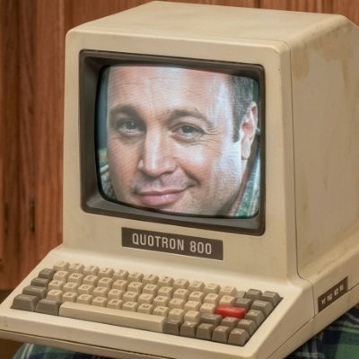 A retro beige desktop computer with a keyboard and monitor displaying a man’s face; the device is labeled “QUOTRON 800.”