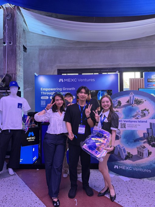 Three people posing in front of a 'MEXC Ventures' booth displaying 'Empowering Growth Through Investment' and 'MEXC Ventures Island' signage.