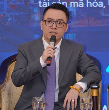 A man in a suit and glasses speaks into a microphone at a panel, with Vietnamese text "tài sản mã hoá" (crypto assets) visible in the background, accompanying a post clarifying that September 1st is not the deadline for closing Binance, OKX, and Bybit in Vietnam but rather a starting point tied to Decree 284's licensing timeline.