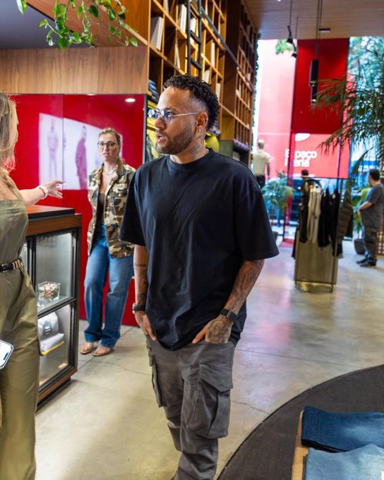 A man with a beard and glasses, wearing a black t-shirt and gray cargo pants, stands inside a PEPP studio while a woman in an olive dress gestures toward him.
