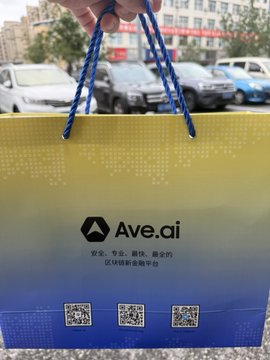 The image features a hand holding a yellow and blue shopping bag with a QR code on it. The QR code contains three small images of toys, which are likely part of an online shopping experience or a promotional campaign for Ave 's June 1st gift box.