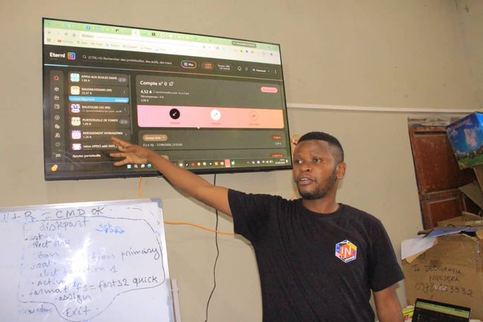 A man in a black t-shirt stands in front of a wall-mounted monitor displaying an Eldorado betting interface, pointing at the screen while a whiteboard with handwritten betting terms sits nearby.