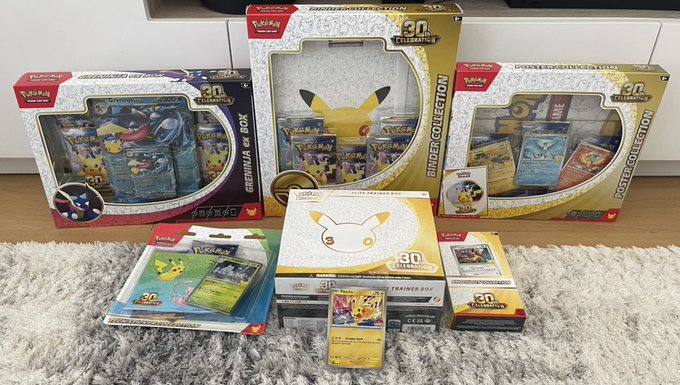 A collection of Pokémon trading card game merchandise, including the 'Greninja ex Box', 'Binder Collection', 'Poster Collection', and various booster packs, displayed on a rug.