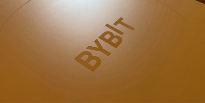 The image shows the "BYBIT" logo printed in dark text on a golden/yellow surface, likely packaging or promotional material. This relates to the post as it represents the Bybit-branded pickleball gear the user received as an airdrop, tying together the company's logo with their offline promotional giveaway.