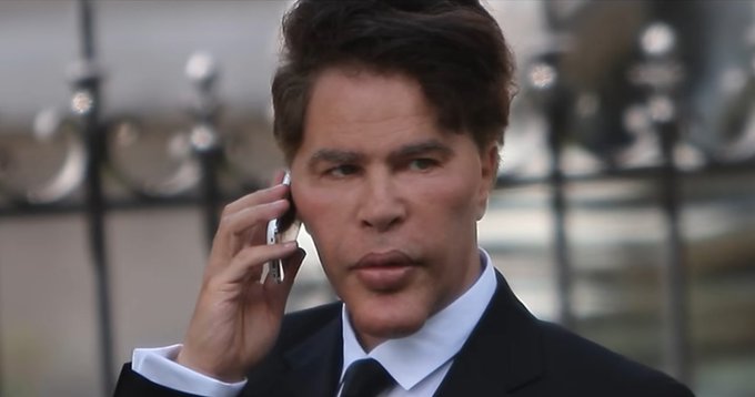 A well-dressed man with tousled brown hair holds a phone to his ear with a serious, contemplative expression, standing before an ornate iron gate. The image of this sharply-attired man receiving a phone call pairs with the post to suggest a powerful figure making a decisive market-moving move — illustrating the caption's point that "he sold" while everyone else tries to explain the rally.