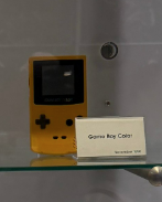 A yellow Game Boy Color is displayed in a glass case with a placard labeled 'Game Boy Color'.