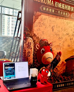 A laptop and coffee sit on a table in front of a Kumamon mascot display at a Rilakkuma 100th City tour exhibition event, with Chinese text reading 'Rilakkuma' and 'limited signature'.