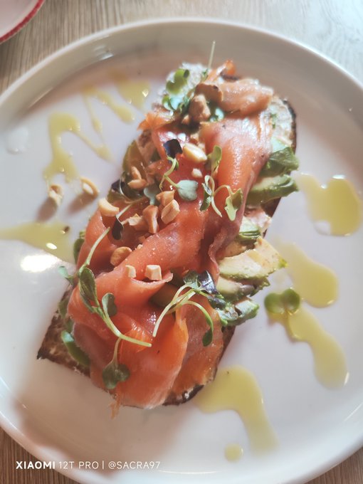 A plated dish of smoked salmon on avocado toast garnished with microgreens and chopped nuts, drizzled with oil, captioned 'XIAOMI 12T PRO | @SACRA97'.