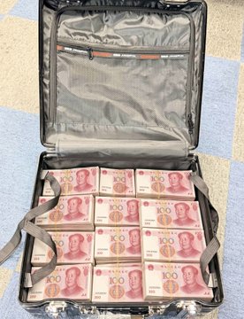 An open suitcase filled with stacks of Chinese 100 yuan banknotes, with an empty mesh pocket on the lid.