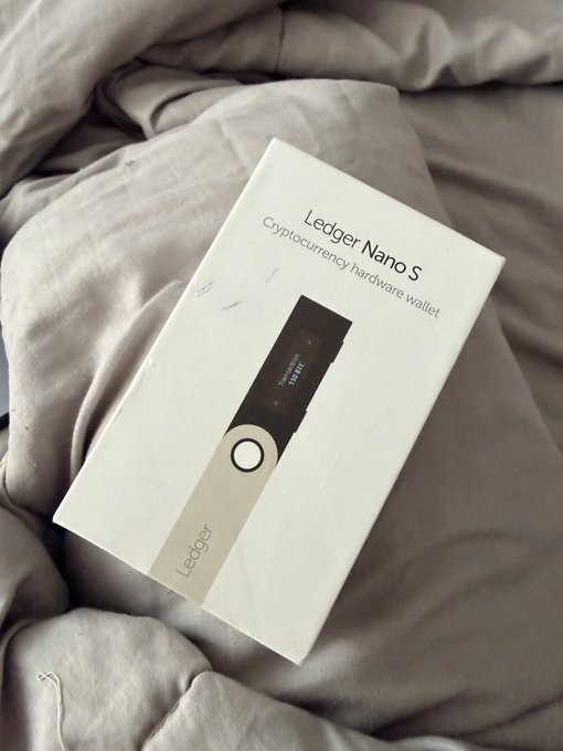 A white retail box for a 'Ledger Nano S Cryptocurrency hardware wallet' resting on a gray fabric surface.